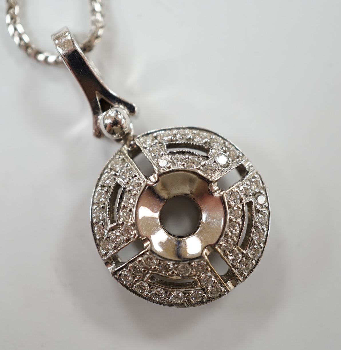 A modern pierced 18k white metal and diamond chip cluster set circular pendant, overall 29mm, gross weight 6 grams, on a 9k white metal chain, 45cm, gross weight 4 grams. Condition - good